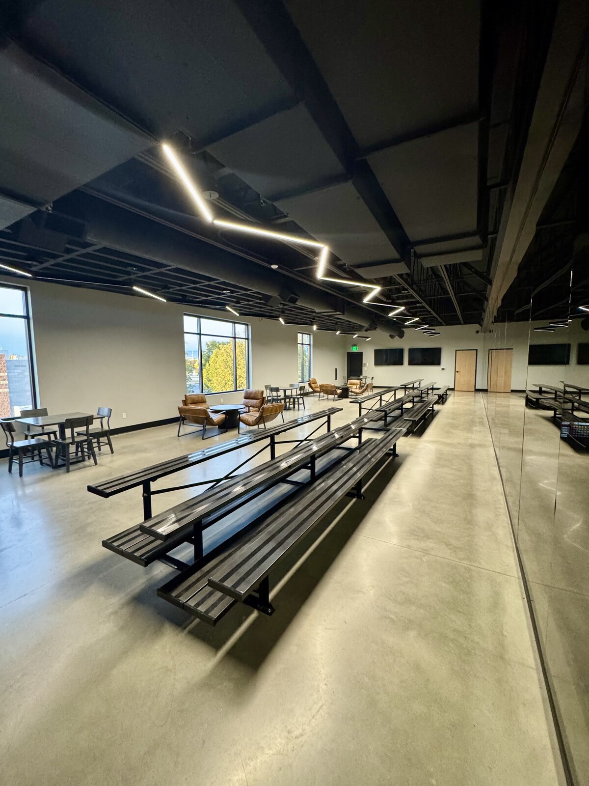 The parent viewing lounge, with tiered black bench seating, a mirrored wall, and tan leather armchairs arranged around small tables beneath zigzagging LED ceiling lights