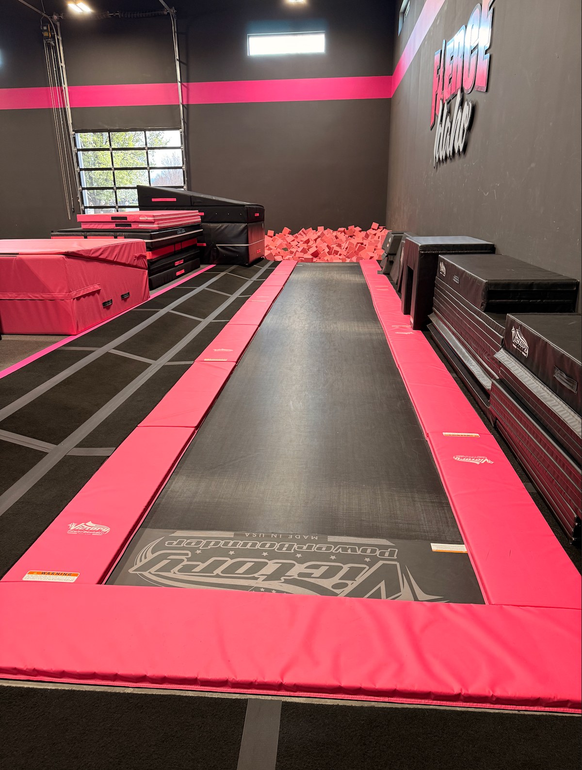 The pink tumble trak running into the foam pit beside stacks of training mats