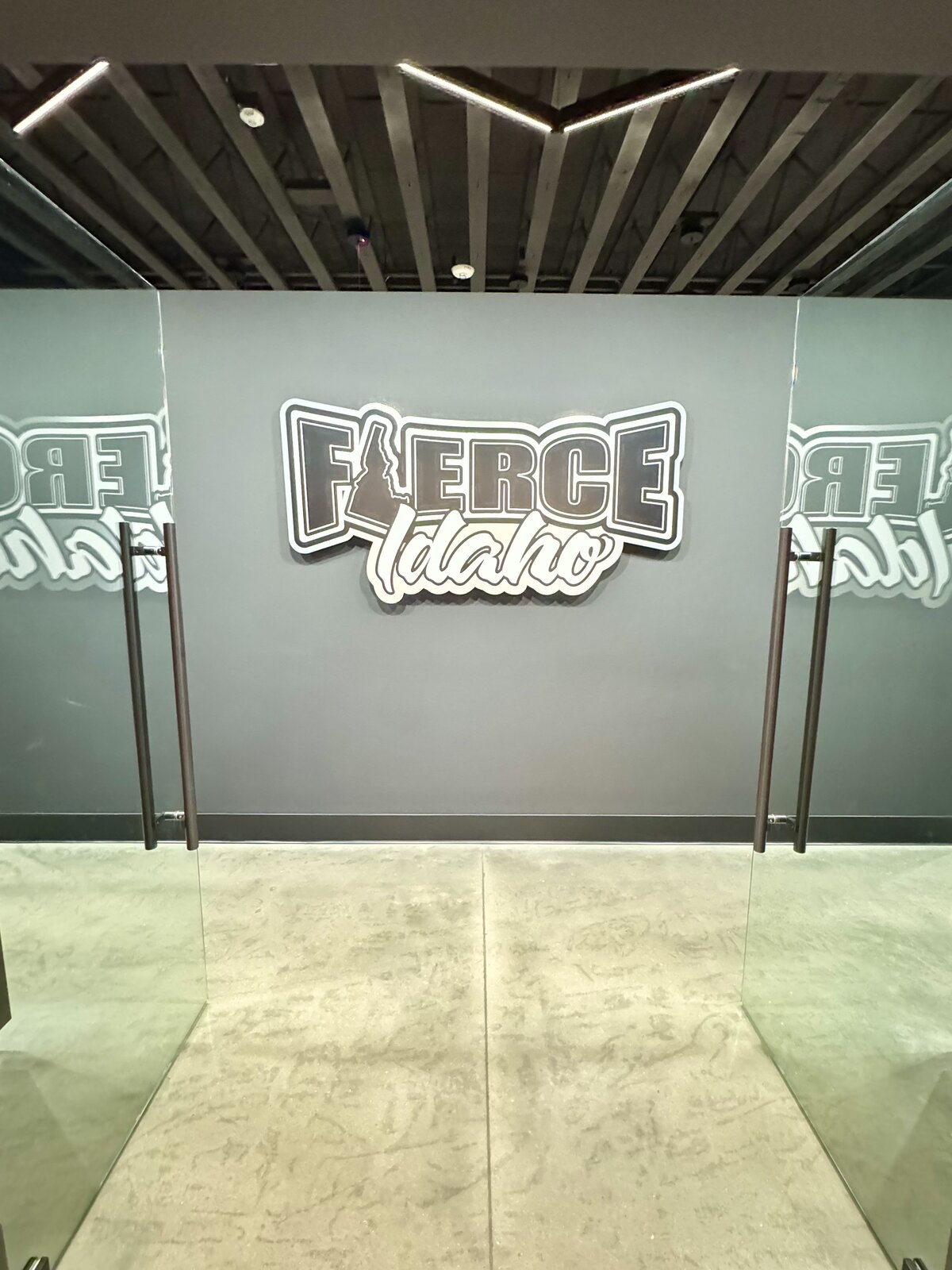 The Fierce Idaho locker room entrance, with glass doors opening onto a matte charcoal wall carrying the FIERCE Idaho sign
